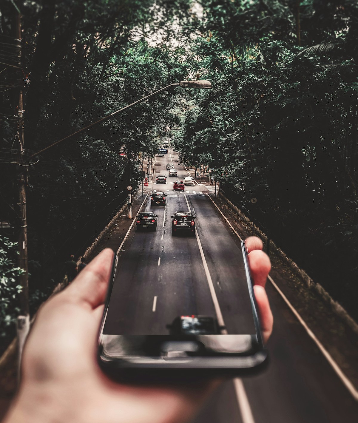 Eine Hand hält ein Handy und auf dem eine Straße mit Autos zu sehen ist. Das Motiv auf dem Display verschmilzt mit dem Foto im Hintergrund.